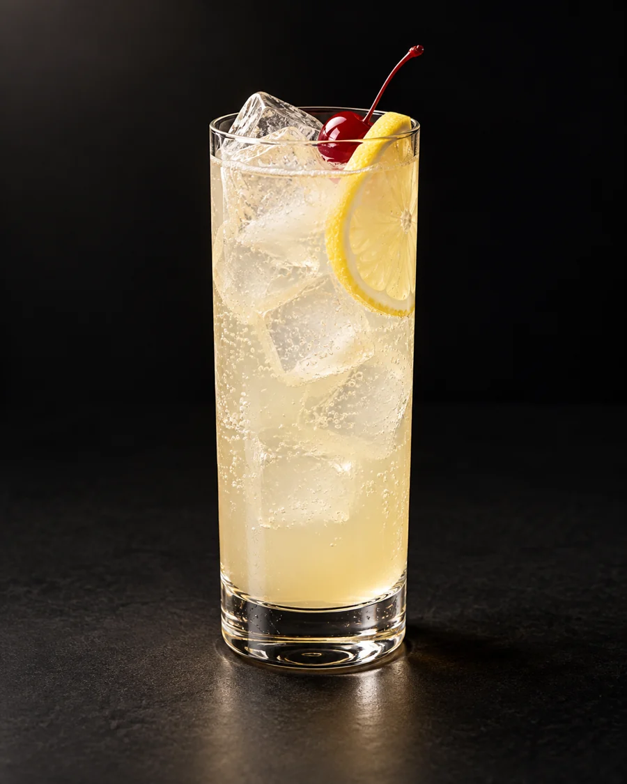 John Collins served in a collins glass with a lemon slice and cocktail cherry against a black background.